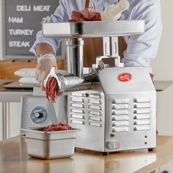 A man using an Avantco meat grinder on a counter in a butcher shop.