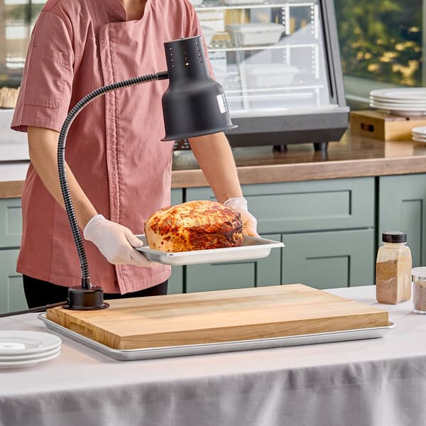 A carving station kit with a 24-inch black heat lamp, cutting board, and drip pan.