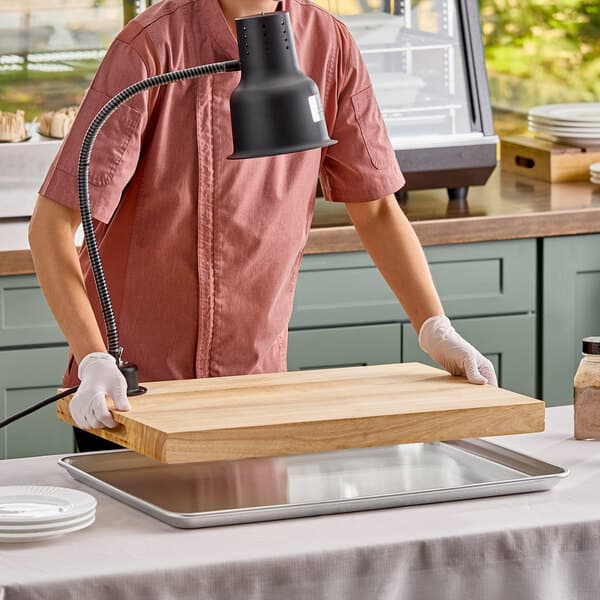 A carving station kit featuring a 24-inch black heat lamp, a wooden cutting board, and a metal drip pan.