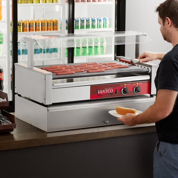 A man using an Avantco hot dog roller grill to cook hot dogs.
