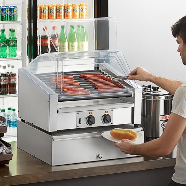 A man using an Avantco slanted hot dog roller to cook hot dogs.
