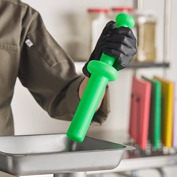 A person in gloves using a green Avantco meat tamper on a counter in a professional kitchen.