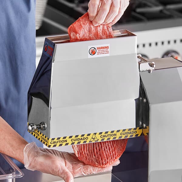 A person using an Avantco meat tenderizer blade set to cut meat on a counter.