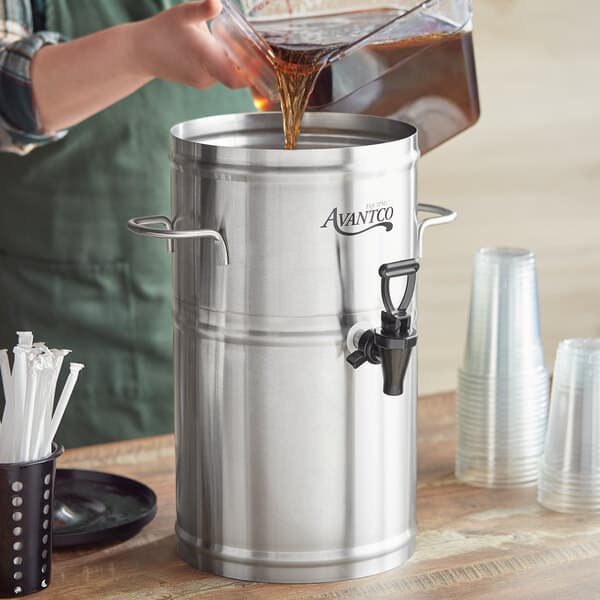 A person pouring brown liquid into a metal container with a white cylinder on top.