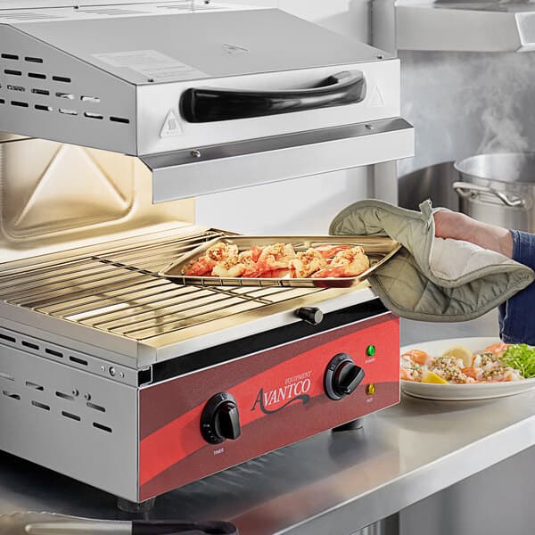 A person using an Avantco electric countertop salamander to cook food on a tray.