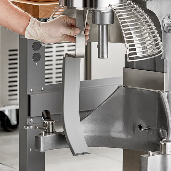 A person wearing a glove uses an Avantco bowl scraper attachment on a mixer.