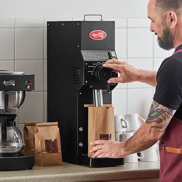A man in an apron using an Avantco bulk coffee grinder on a counter in a professional kitchen.