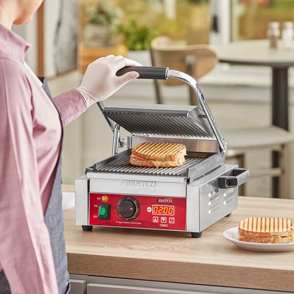 A person using an Avantco commercial Panini grill to make a sandwich.