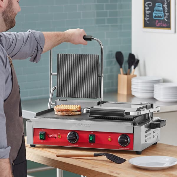 A man in an apron using an Avantco commercial dual panini sandwich grill to cook a sandwich.