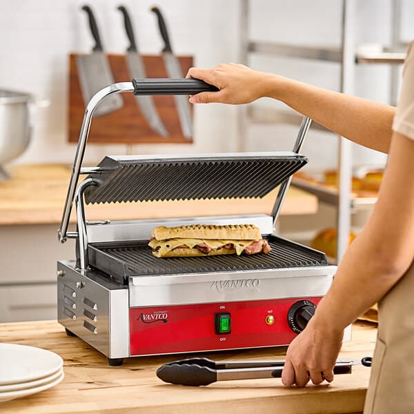 A person cooking a sandwich on an Avantco commercial panini grill.