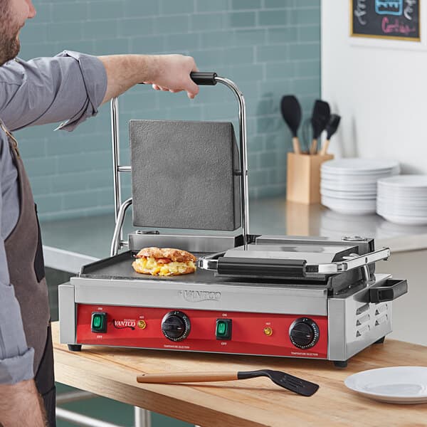 A man cooking a sandwich on an Avantco commercial panini grill.