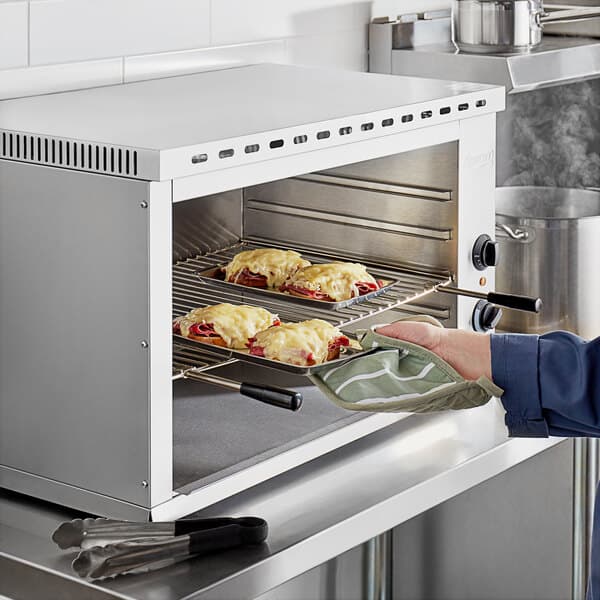A person using a glove to put food in an Avantco countertop cheese melter.