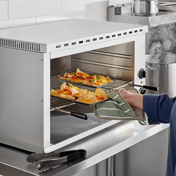 A woman using an Avantco electric countertop cheese melter to melt cheese on nachos.