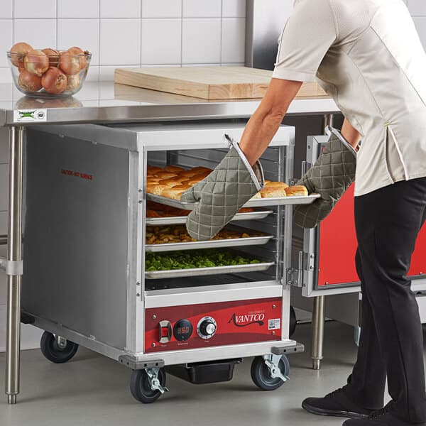 A man in a chef's outfit putting food into an Avantco heated holding cabinet.