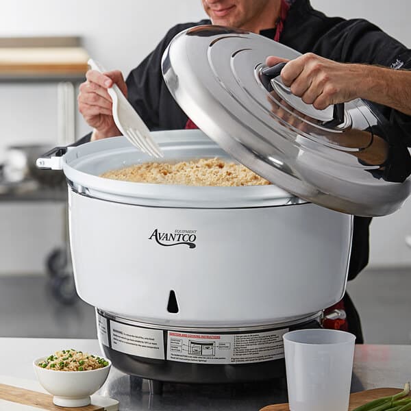 A man using an Avantco natural gas rice cooker to cook rice in a large white pot.