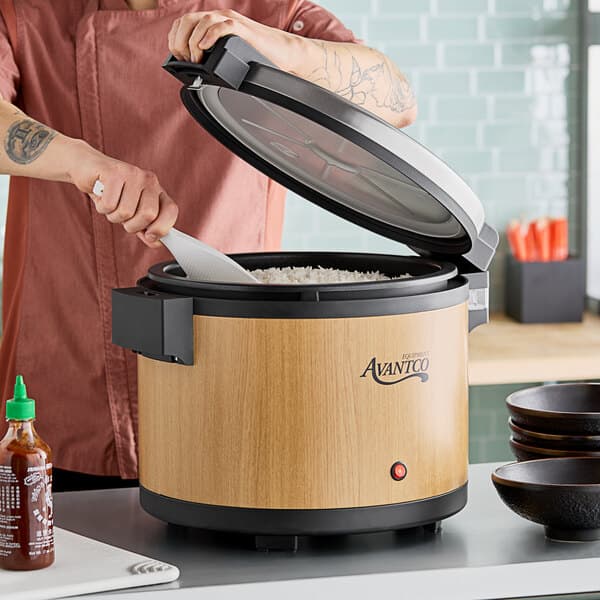 A man using an Avantco woodgrain electric rice warmer to cook rice on a counter.