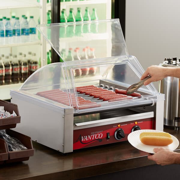 A person using tongs to put hot dogs in an Avantco hot dog roller grill.