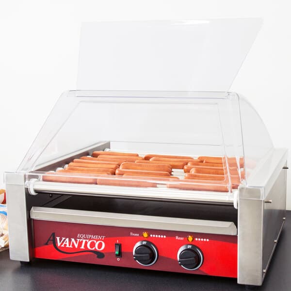 An Avantco hot dog roller grill with hot dogs cooking on it and a sneeze guard.