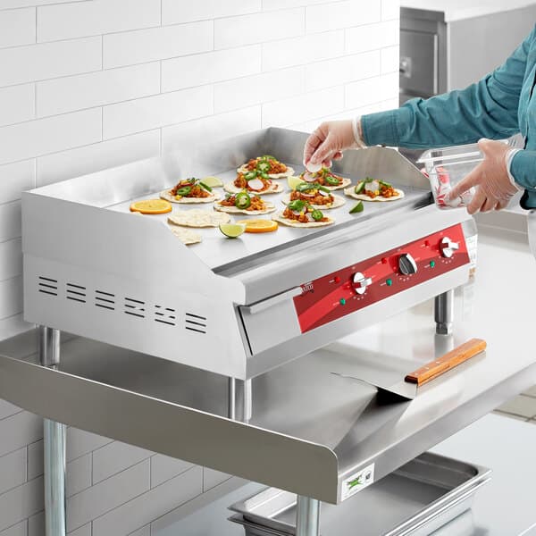 A stainless steel 30-inch electric countertop griddle with food being prepared on its flat cooking surface.