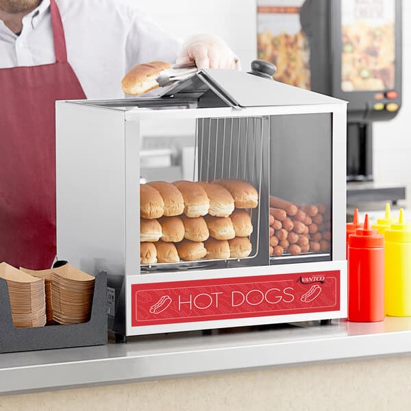 A man using an Avantco hot dog machine to steam hot dog buns.
