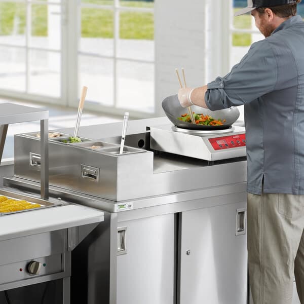 A man cooking food on an Avantco stainless steel omelet / pasta station base in a commercial kitchen.