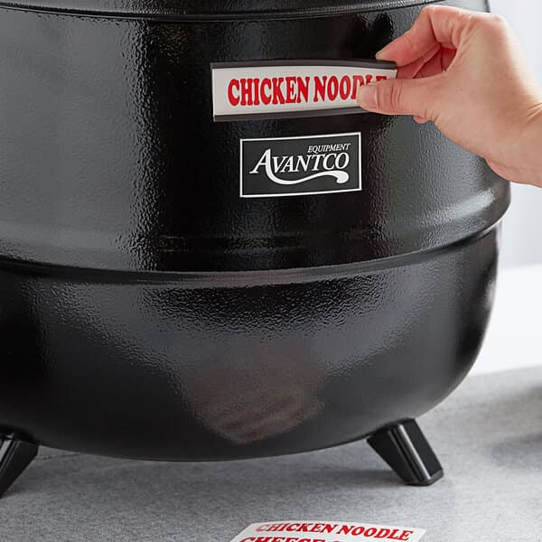 A hand putting a sticker on a black soup kettle.