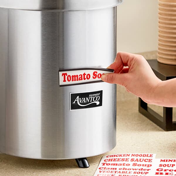 A hand putting a label on an Avantco stainless steel warmer on a hotel buffet counter.