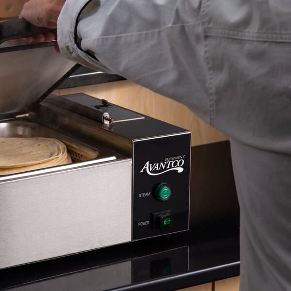 A person using an Avantco countertop steamer to cook tortillas.
