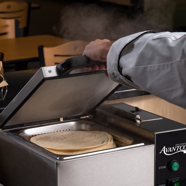 A person using an Avantco countertop steamer to prepare tortillas.