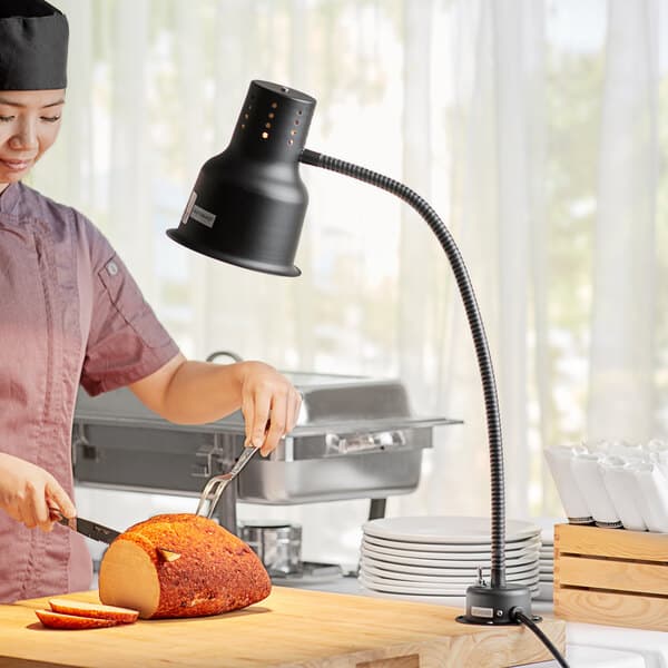 A woman cutting a piece of bread with an Avantco black countertop bulb warmer.