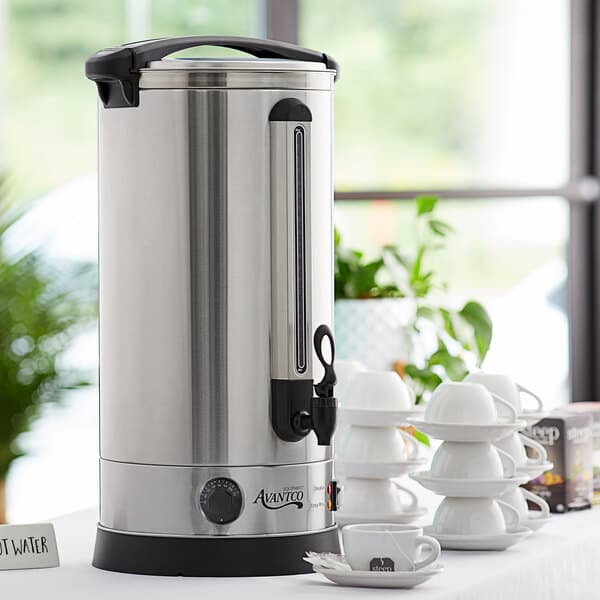 An Avantco water boiler on a table with cups and saucers.