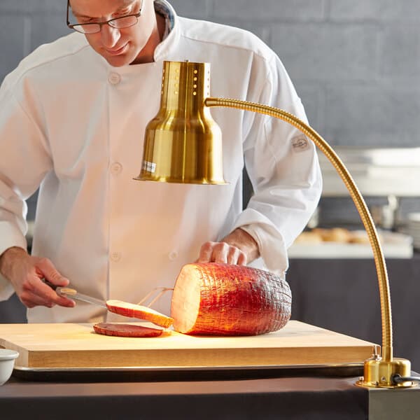 An Avantco stainless steel heat lamp with a gold arm being used to cut meat.