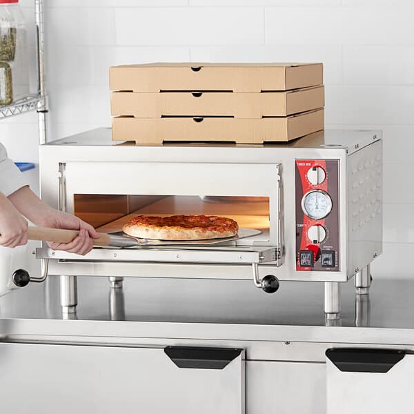 A person placing a pizza in an Avantco countertop pizza oven.