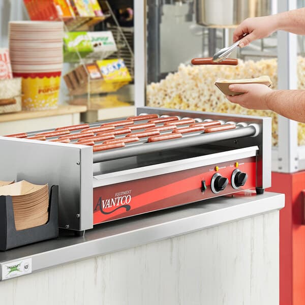 A man using silver tongs to prepare hot dogs on an Avantco hot dog grill.
