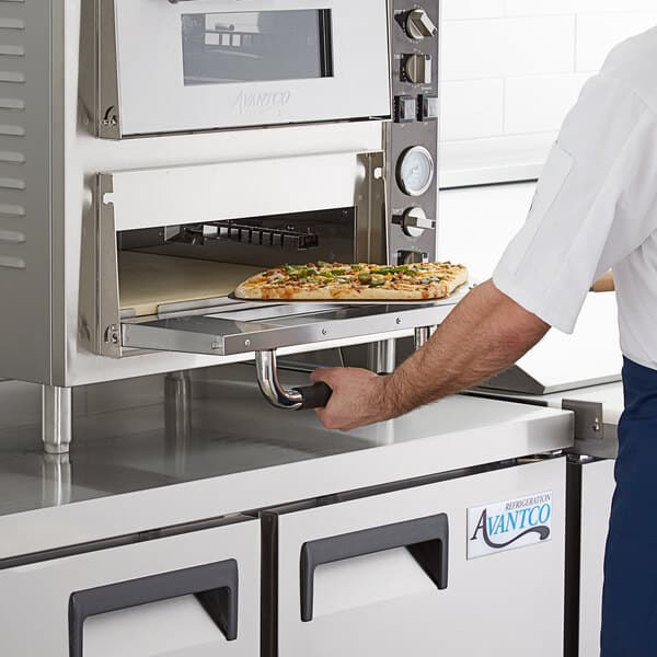 A man using an Avantco countertop pizza oven to cook a pizza on a square pizza stone.