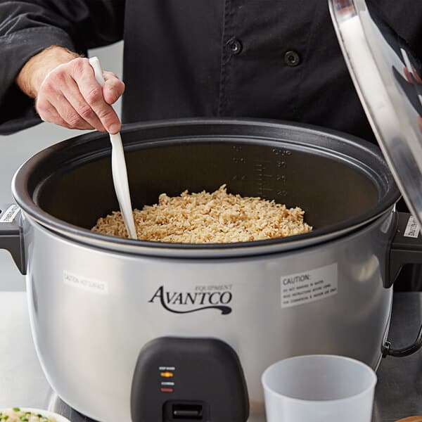 A person stirring rice in an Avantco rice cooker.