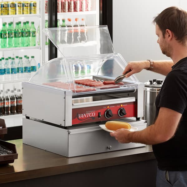 A man using an Avantco hot dog roller to cook hot dogs.