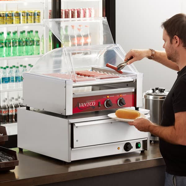 A man using an Avantco hot dog roller to cook hot dogs.