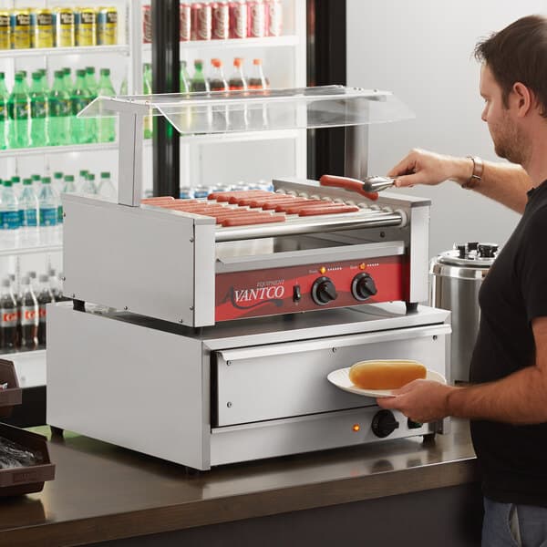 A man using an Avantco hot dog roller grill to cook hot dogs.