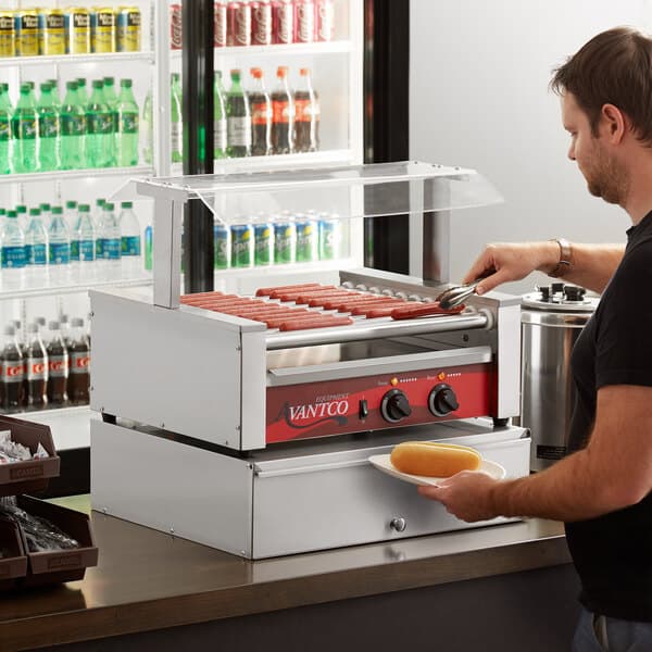 A man cooking hot dogs on an Avantco hot dog roller grill.