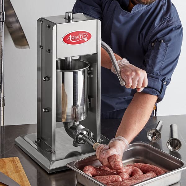 A man using an Avantco stainless steel vertical manual sausage stuffer to make sausage.