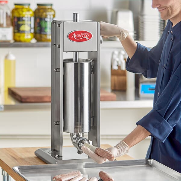 A man in a blue uniform uses the Avantco stainless steel sausage stuffer on a counter.