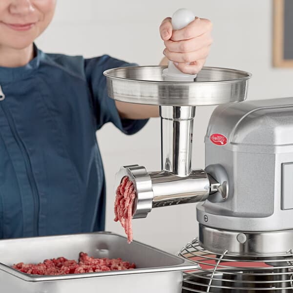 A woman using an Avantco meat grinder attachment to grind meat.