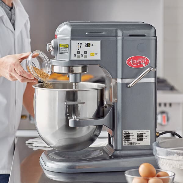 A woman using a dark gray Avantco countertop mixer to mix brown powder, flour, and eggs in a bowl.