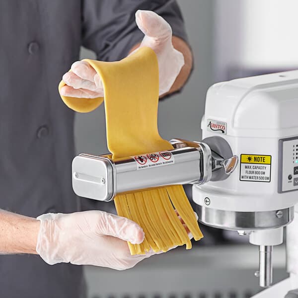 A person using an Avantco pasta roller / cutter attachment to make pasta with a mixer.