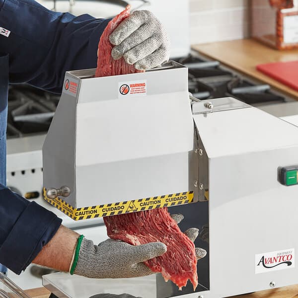 A person using an Avantco meat tenderizer to cut meat on a counter.