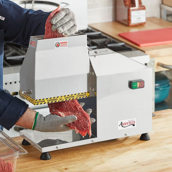 A man using an Avantco meat tenderizer on a counter in a butcher shop.
