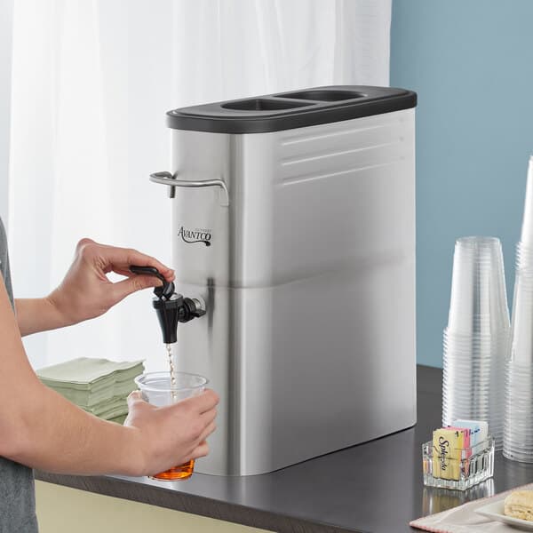 A person pouring iced tea from an Avantco Slim Iced Tea Dispenser into a glass.
