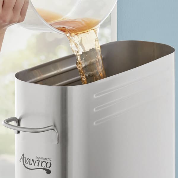 A person pouring iced tea into a stainless steel Avantco dispenser.