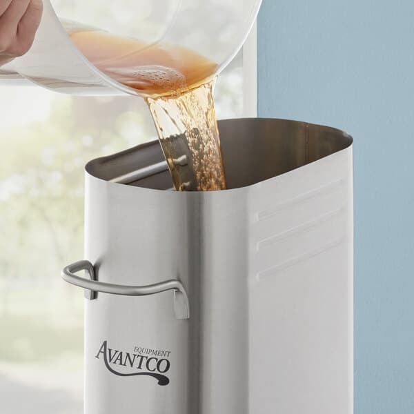 A person pouring brown liquid into an Avantco stainless steel iced tea dispenser.